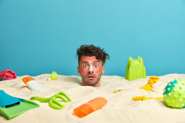 young-man-head-with-sunscreen-cream-face-surrounded-by-beach-accessories